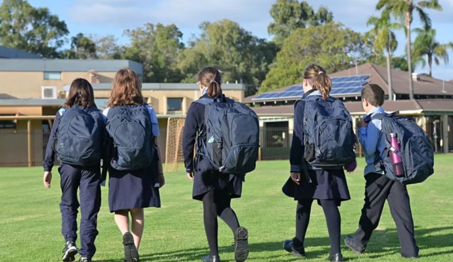 Five children walking across a school playing field
